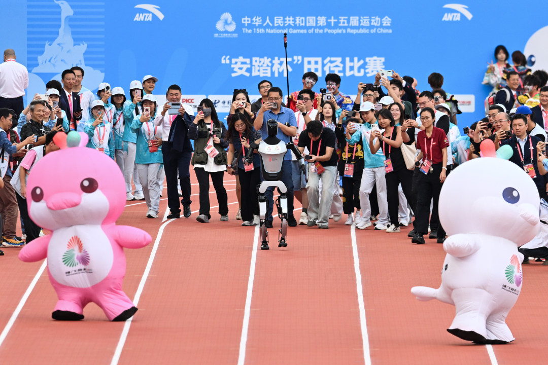 2025年11月17日,广东奥林匹克体育中心,十五运会田径项目,十五运会田径项目,十五运会吉祥物与机器人“Walker”进行赛跑,受到记者热捧。