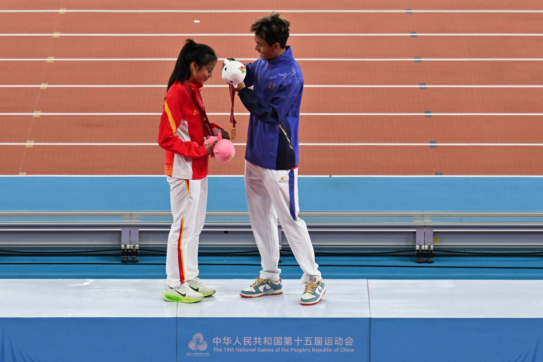 2025年11月16日,广东奥林匹克体育中心,十五运会田径项目,4×100米混合接力颁奖仪式,夺冠的福建选手何锦櫶(右)为四川选手刘峡君(左)戴上自己的金牌。