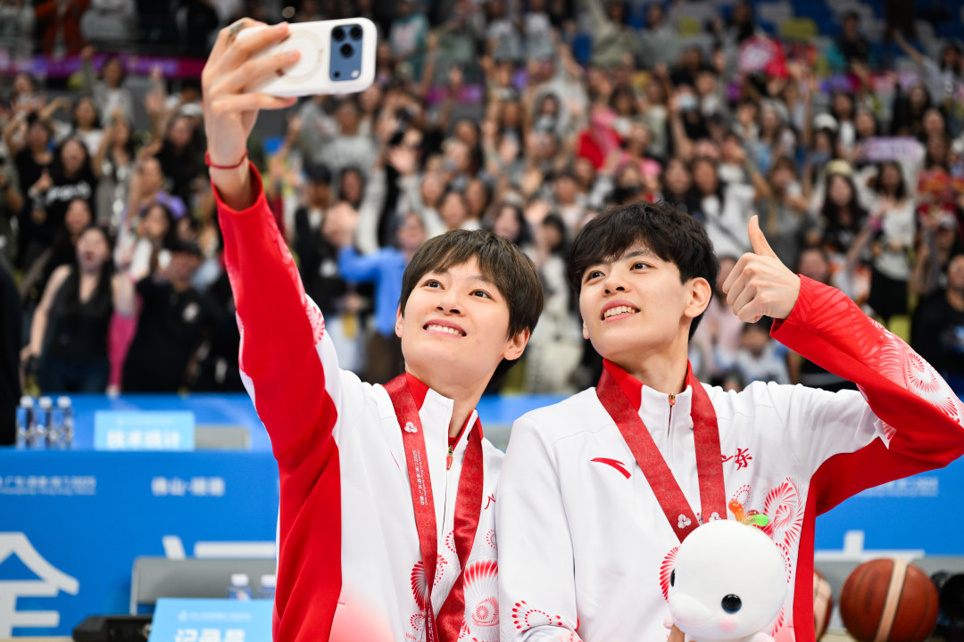 2025年11月15日,佛山市顺德区德胜体育中心,十五运会女篮成年组决赛广东对阵四川,夺冠的广东队员杨舒予(右)、杨力维(左)与现场观众自拍。