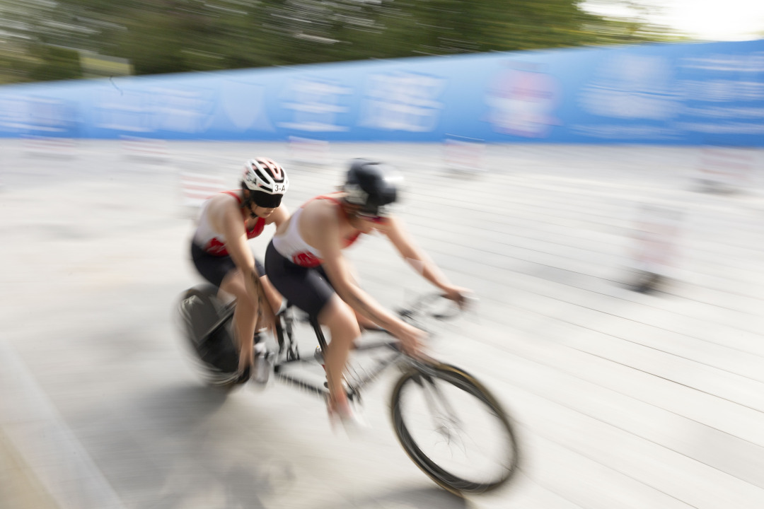 视障运动员在引导员的带领下完成骑行环节比赛。