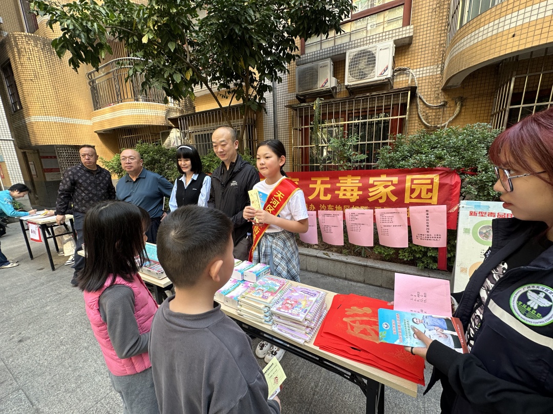 沙东街党工委副书记陈波、平安法治办主任李福泉、学生宣讲员在摊位前宣传禁毒知识。