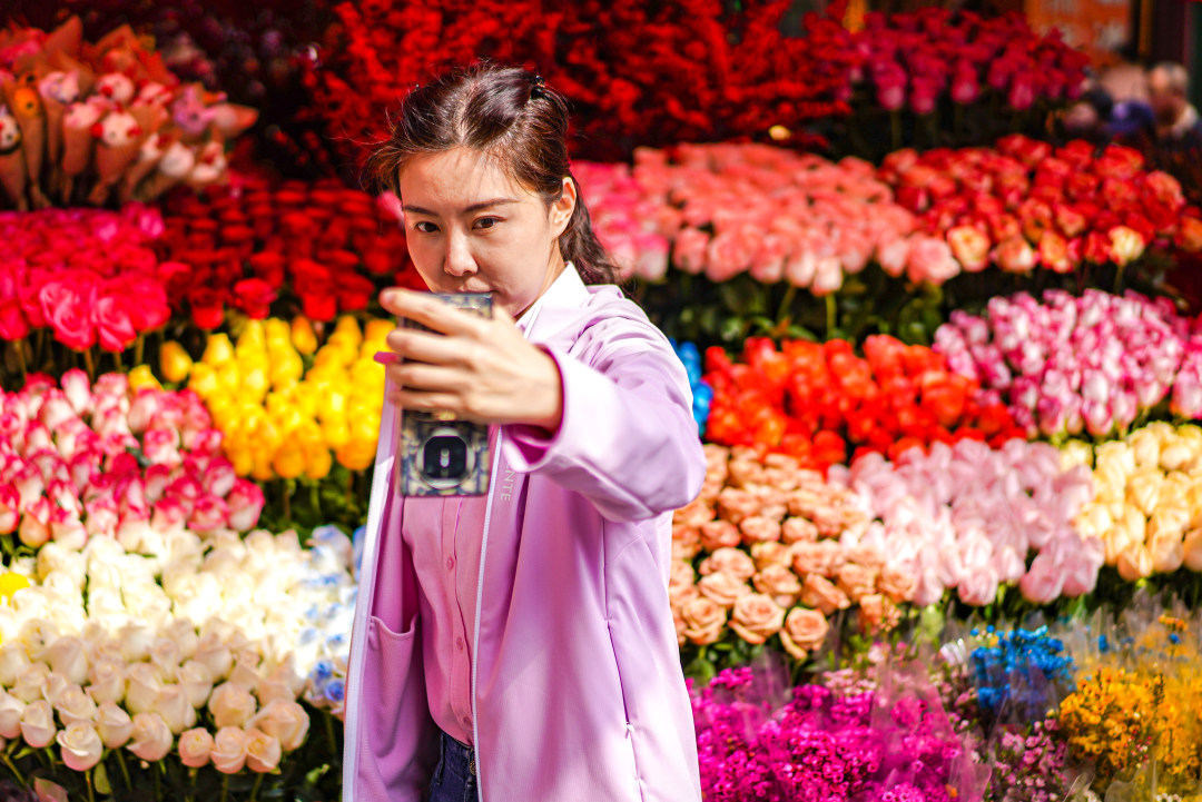 女生以花市五彩斑斓的鲜花为背景自拍。