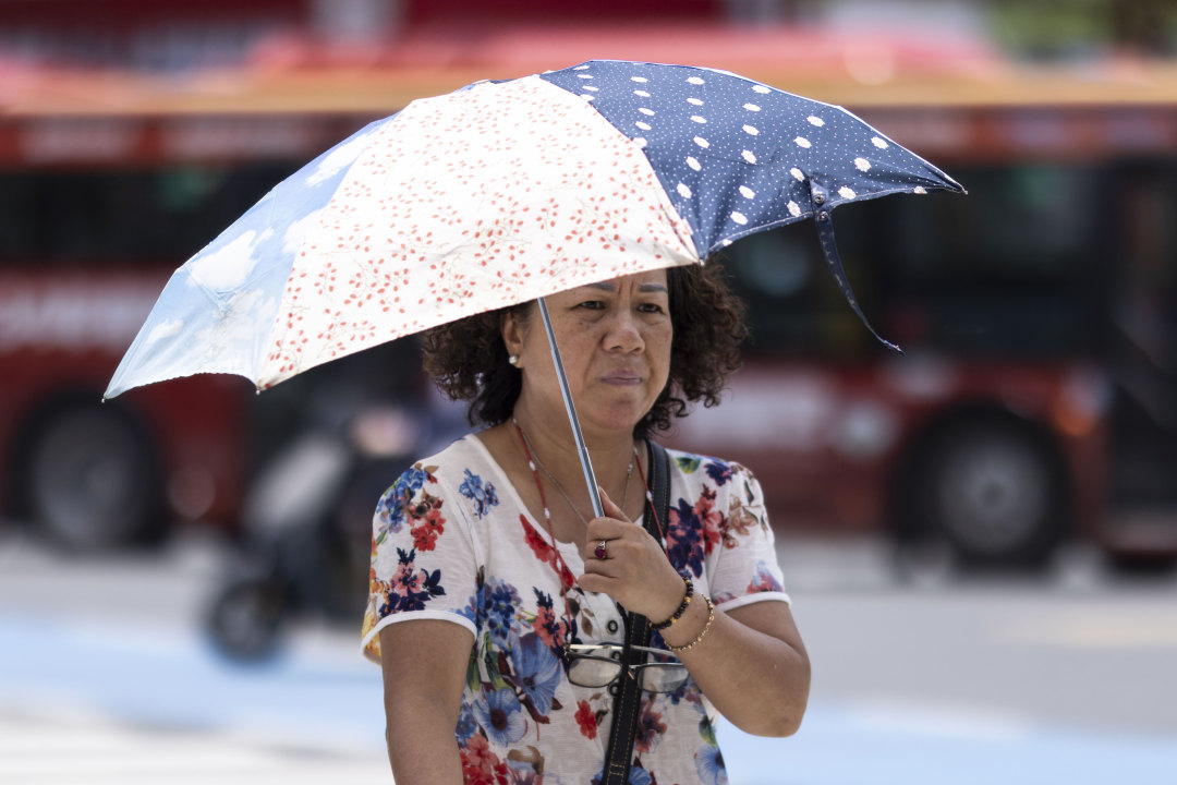 市民撑伞在阳光下过马路。