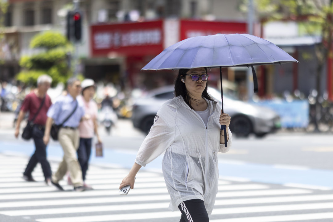 市民撑伞在阳光下过马路。