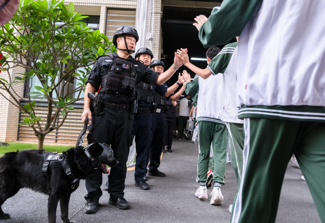 广州市培英中学云城校区考场,维持考场秩序的特警们带着警犬,跟考生们击掌加油,祝大家高考“旺旺”。考生们开心地跟帅气警犬互动。