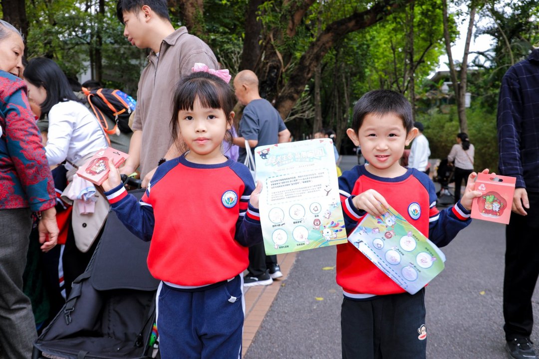 在动物园北门领奖区,孩子们兴奋地从工作人员手中接过全运主题的文创纪念品。(通讯员供图)